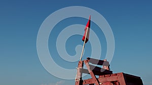 Red flag on a wooden rescue tower. Symbol of danger. A flag prohibiting swimming on the beach. Restrictions.