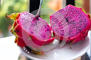 A red-fleshed dragon fruit cut in half with a spoon stuck in. Exotic tropical fruits