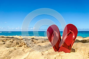 Red flip flops in heart shape on the sandy beach