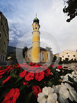 Red flower bouquet view of yellow Heiliger Antonius church chapel in Lienz East Tyrol Austria alps Europe