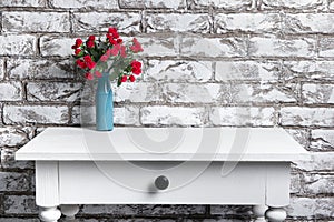 Red flowers in vase on the table on black and white brick wall background