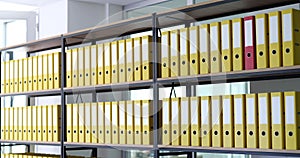 Red folder moves on shelves in row of identical yellow ones in archive