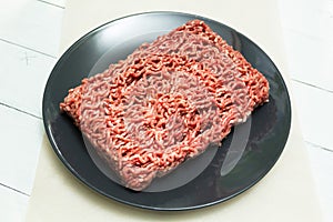 Red forcemeat on a black plate on a white wooden table