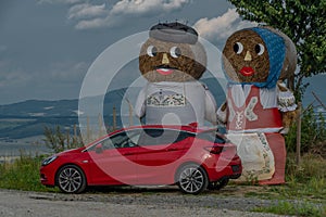 Red fresh car with hay puppets in field in summer hot day