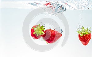 Red fresh fruit strawberries falling into water with splash on white background, strawberry for health and diet, nutrition