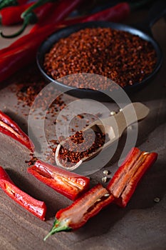 Red fresh hot chilli peppers with green tails and dried red chilli flakes in bowl on wooden board