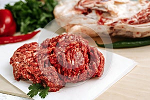 Red fresh minced meat on the background of lamb legs, red pepper and greens. Ground beef on the background of fresh meat in the