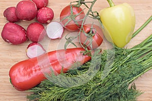 Red fresh radish, tomato, green and red pepper and green dill on wooden kitchen board