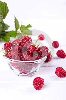 Red fresh raspberries in a glass bowl with green leaves