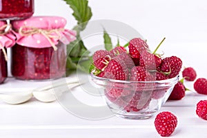 Red fresh raspberries in a glass bowl with green leaves