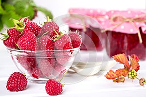 Red fresh raspberries in a glass bowl and Raspberry jam with green leaves