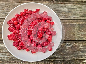 Red fresh raspberries on rustic wood background. Bowl with natural ripe organic berries with peduncles on wooden table