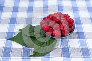 Red fresh raspberries on white rustic wood background. Bowl with natural ripe organic berries with peduncles and green