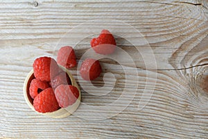 Red fresh raspberries are in the wooden cup and on the wooden background. Healthy raspberries