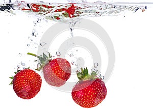 Red fresh strawberries thrown into the water, under water. Spat and splash