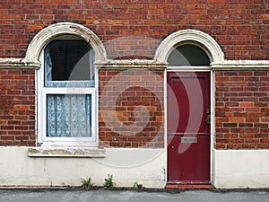 Red front door and window of a typical old brick british terraced house with shabby peeling paintwork