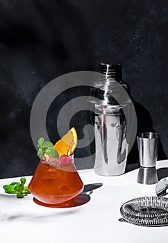 Red fruit cocktail drink with rum, pineapple juice, ssrop, orange, mint, cocktail cherry and ice. Gray and white background, hard