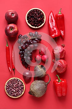 Red fruits and vegetables on a red background. Pomegranates, dried cranberries, paprika, cappy peppers, radishes, grapes