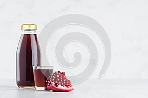 Red garnet juice in glass bottle mock up with wine glass, fruit slice on white wood table in light interior, template.