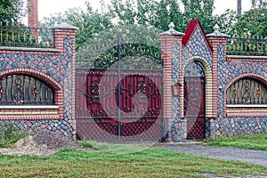 Red gate and a door made of metal with a forged pattern and a stone fence in the street