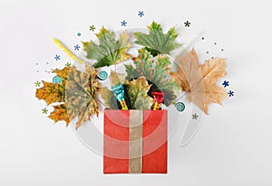 Red gift box with autumn leaves, party confetti and noisemakers