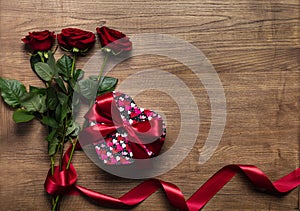 Red gift box with beautiful red ribbon and roses isolated on wooden background