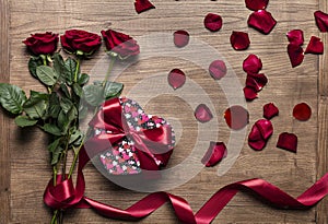Red gift box with beautiful red ribbon and roses isolated on wooden background