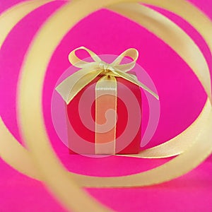 Red gift box at the end of the spiral yellow ribbon, fuchsia background, square.