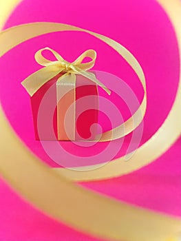 Red gift box at the end of the spiral yellow ribbon, fuchsia background, vertical.