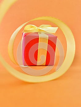 Red Gift box at the end of the spiral yellow ribbon, orange background, vertical.