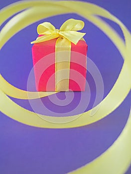 Red Gift box at the end of the spiral yellow ribbon, purple background, Vertical.