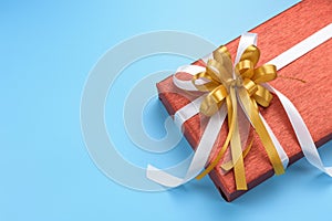 Red gift box with gold and white ribbon bow on blue background