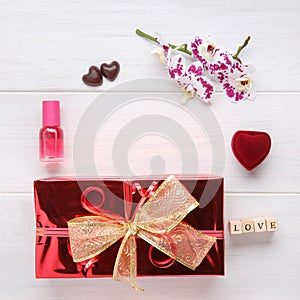Red gift box with golden ribbon bow and orchid flower on white wooden table. Top view. Flat lay. Copy space