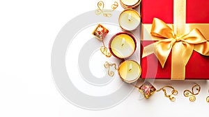 Red gift box with golden ribbon, chocolate sweets and candles on white background