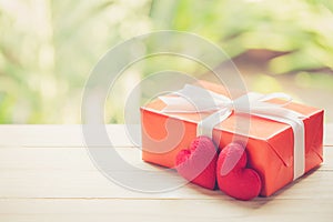 Red gift box and heart shape on wood table top with nature green blur bokeh background