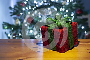 Red gift box with lighted green lace and christmas tree with christmas lights in the background