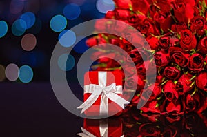 Red gift box and red roses bouquet on table with colorful city bokeh lights