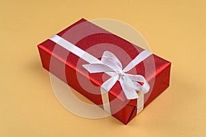 Red gift box with ribbon and bow on golden background, copy space. Holiday greeting card. Mothers day, birthday.