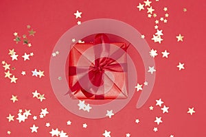 Red gift box with ribbon bow on red background and golden sparkling conffeti. Free space for your text