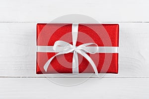 Red gift box with ribbon and bow on white wooden background, copy space. Holiday greeting card. Mothers day, birthday, Womens Day