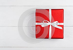 Red gift box with ribbon and bow on white wooden background, copy space. Holiday greeting card. Mothers day, birthday, Womens Day