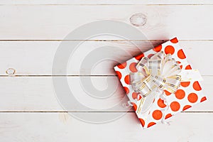 Red gift box with ribbon on white background on white wooden background with copy space, top view.