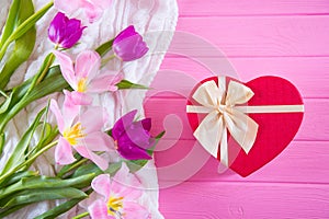 Red gift box in shape of heart and tender bouquet of beautiful tulips on pink wooden background