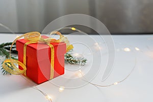 Red gift box tied with gold ribbon on a light table with bokeh lights and blurred background