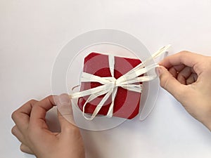 Red gift box with white bow on white background and hands holding ribbons