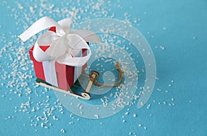 Red gift box with white ribbon and bow on a sled on a blue background. Christmas and New Year concept. Copy space. Postcard.