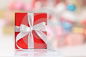 A red gift box with white ribbon on the table and blurred backgrounds for any holiday concept
