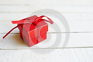 Red gift box on white wooden background with copy space, surprise for birthday, christmas, or valentine`s day