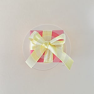 Red gift box with yellow ribbon on off white background. Square, aerial.