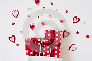 Red gift boxes peek out of a white paper bag next to many different hearts